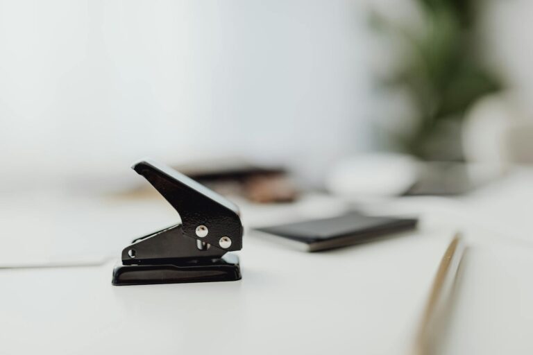 Close-up of a black hole puncher on a clean white desk in a minimalist office setting.